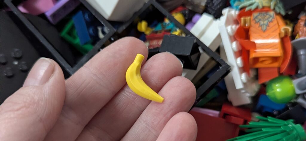 A person holds a banana piece of Lego in their fingers